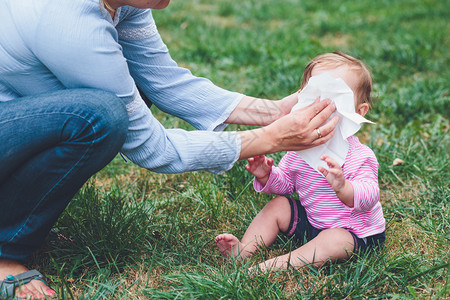 蹲在草地上给婴儿擦鼻涕洗脸的母亲图片