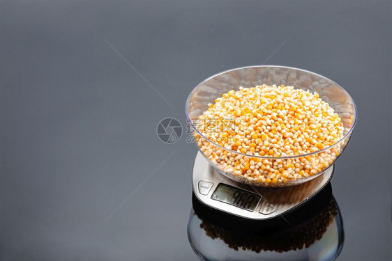 展示以不锈钢电子规模灰面镜底背景在不锈钢电子尺度上透明的碗中玉米以电子规模灰面脸和复制空间的形式将玉米放在碗里体积准备图片