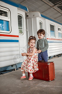 美丽的在小火车站穿着旧衣服和式手提箱的男女小孩和少情绪白种人图片