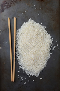 铺设食物桩金属烘烤板上一堆未煮熟的稻谷粒高角镜头在谷物垂直格式旁边躺着一对筷子图片