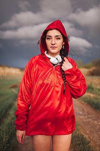 放松鸡皮疙瘩夏天年轻女子在雨与衣和耳机一起站在田地上图片