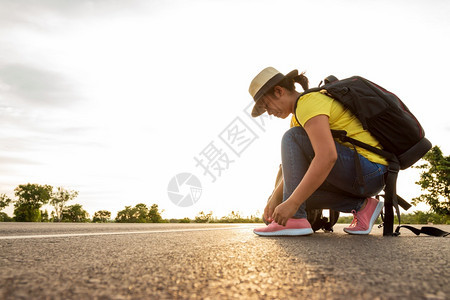 皮革乐趣美丽的女游客在高速公路上用太阳的金光背包概念把运动鞋绑在公路上图片