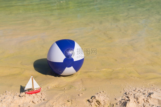 夏天温暖的玩具船和在水上漂浮的充气蓝白海滩球图片