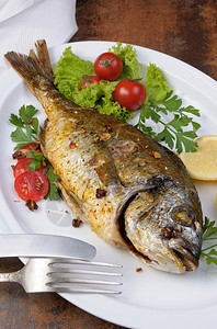 切片多拉和盘子上加蔬菜醋和柠檬片的烤鱼一种晚餐图片