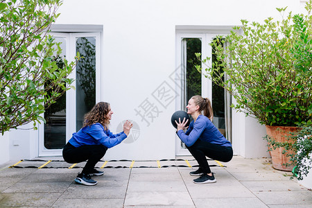 卫生保健康教练员两个女青年在露台和药球一起锻炼两个女青年在阳台上图片