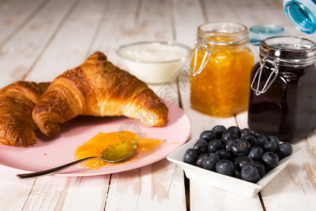 新鲜早晨餐与牛角面包蓝莓酸奶和果酱在木制桌边早餐与羊角面包在木制桌边食物图片