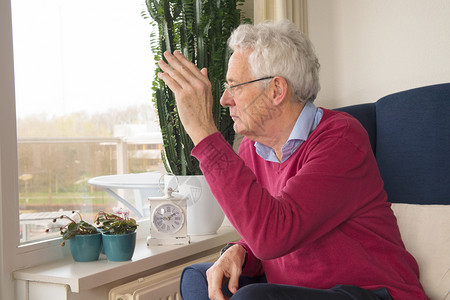 60摄氏度老年人独自的灰色高官一个人坐在椅子上和外面的人挥手告别