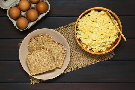 用木碗中的蛋和芥子酱配制的新鲜自鸡蛋沙拉盘子里有一片全谷物面包箱里有鸡蛋用天然光照在黑木头上饮食物图片