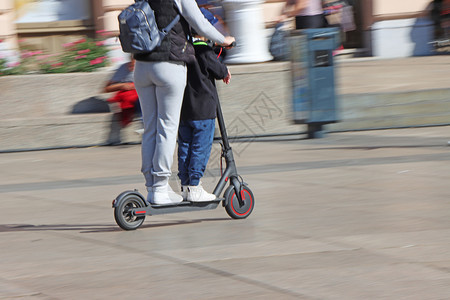 电动滑板车当代的臭鼬母亲和儿子在市广场乘坐电动脚踏车运模糊图片