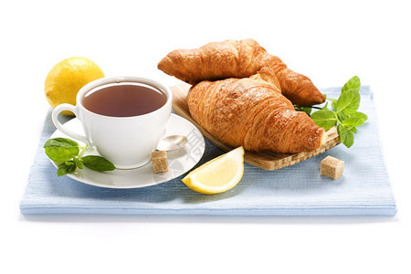 热的自然茶点蓝餐巾纸上的草药茶薄粉柠檬和羊角面包图片