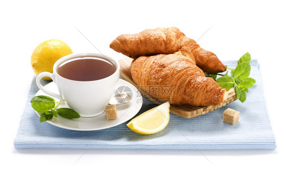 热的自然茶点蓝餐巾纸上的草药茶薄粉柠檬和羊角面包图片