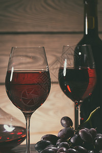 两杯和一瓶红酒葡萄在桌子上色调两杯和一瓶红酒葡萄在桌子上满的红色复制图片