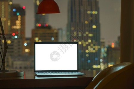 摩天大楼正面小样白桌上的膝型计算机显示在夜晚背景下查看整个城市图片