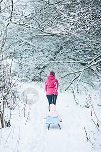 在森林中散步时妇女与儿一起拉滑雪车家庭父母闲暇图片