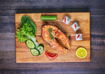 含蔬菜和大米的灰鲑鱼在木板和生锈桌上加蔬菜和大米芹香盘子图片