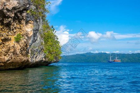 天空晴自然印度尼西亚热带岛屿的岩礁海岸天气晴朗雨林位于落基海岸远处的山坡游艇上有雨林和远距离游艇图片
