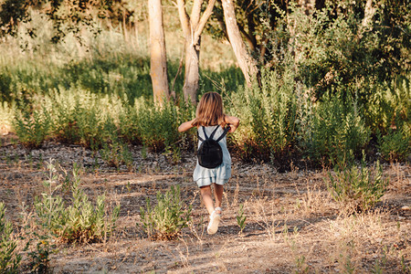 金发年轻女孩在田里跑身着洋装手握放大玻璃杯背包人们树木跑步图片
