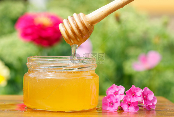 花粉蜜蜂有机的木制桌上蜜罐棍子和粉红色花图片
