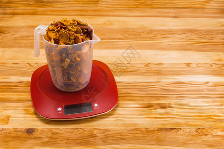 天然木质背景上红色塑料电子秤上透明量杯中的干苹果复制空间木质背景上电子秤量杯中的干苹果厨房电子的措施图片
