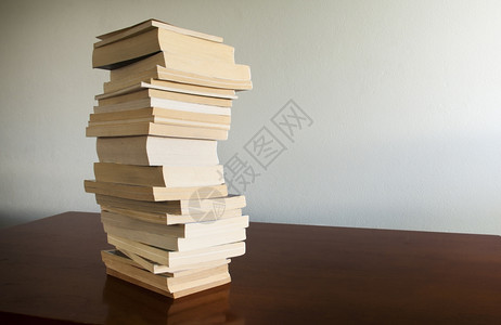 在后面大量书本堆积在一块木材桌面上后空着白书柜信息图片