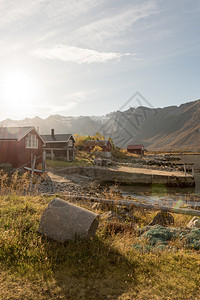 景观岛天在挪威特罗姆索海岸的一座小屋上山峰顶在景色优美的农村风景中闪耀着光亮的束和透照明图片