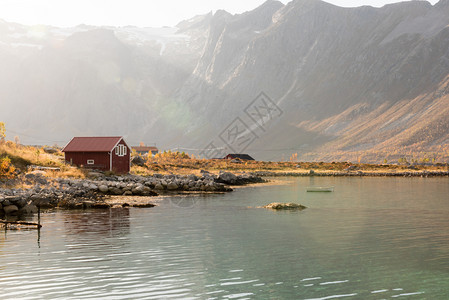 海岸线在挪威特罗姆索海岸的一座小屋上山峰顶在景色优美的农村风景中闪耀着光亮的束和透照明水安宁图片