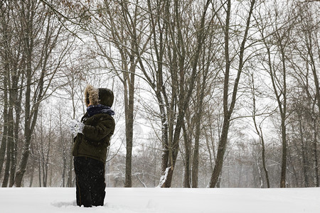 父母一名身着温暖衣服在冬季与雪男孩玩耍的小在暴风雪中走冬季公园里快乐的户外图片