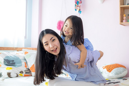 快乐的亚洲小女孩在她母亲的背上在房子里人们美丽的成图片