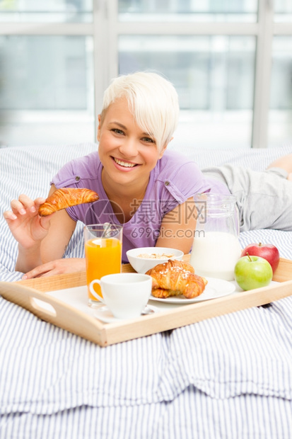 早晨白色的肖像年轻金发女美在卧室吃早餐图片