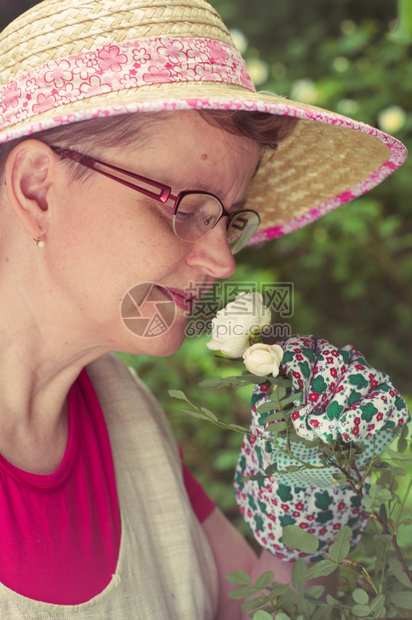 在花园里闻着白玫瑰的成熟女人交叉图像处理过夏天微笑快乐的图片