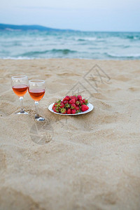 两杯酒和一盘草莓在沙滩上海边野餐两杯酒和一盘草莓在沙滩上海边野餐新鲜的水果派对图片
