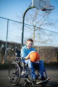 玩积极的减值坐在轮椅上的青少年男孩在户外法庭上打篮球的肖像图片
