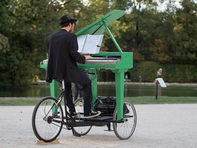 上市乐趣雕像在公共园里玩绿色移动钢琴的持帽子手图片