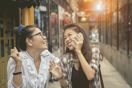 幽默亚裔两个洲女在购物街上使用智能电话并大笑的快乐情感笑声幸福放松图片