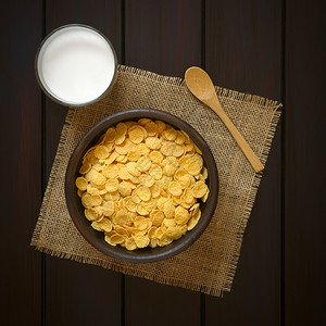 脆皮的健康烤玉米片在生锈碗中早餐谷类边上加一杯牛奶和木勺子用自然光照黑木头图片