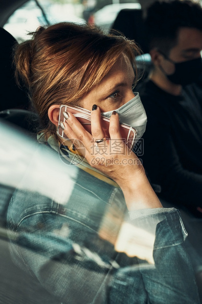 技术坐着一种妇女用智能手机在一辆戴面罩的汽车里通过电话交谈以避免感染防止疾病在出现冠状腺毒时传播b使用智能手机坐在车内戴着面罩的图片
