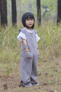 身着棉衣服装和羊毛兜帽的亚裔可爱儿童肖像他们站在松木中立望着照相机的眼睛接触户外张贴孩子图片