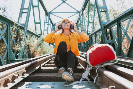 冒险妇女在废弃的铁路桥上用耳机听音乐和收羊毛落下图片