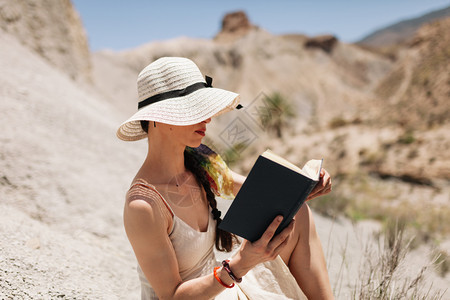 帽子年轻女孩在看一本书穿着白色衣服在沙漠里坐着座位女士放松图片