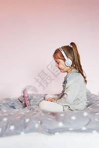 快乐的学龄前儿童小女孩学龄前幼童习网上解谜游戏玩教育单盘在大流行病检疫期间在家里使用平板电脑和耳机发出声音坐着图片