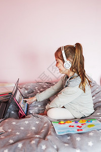 小女孩学龄前幼童习网上解谜游戏玩教育单盘在大流行病检疫期间在家里使用平板电脑和耳机发出声音孩子移动的坐着图片