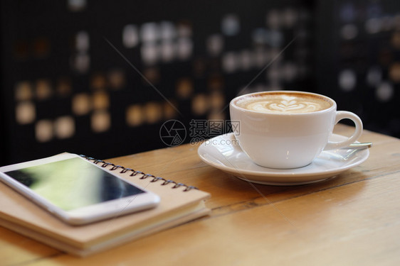 咖啡店用智能手机在木桌上配有拿铁艺术的白色咖啡杯食物卡布奇诺香气图片