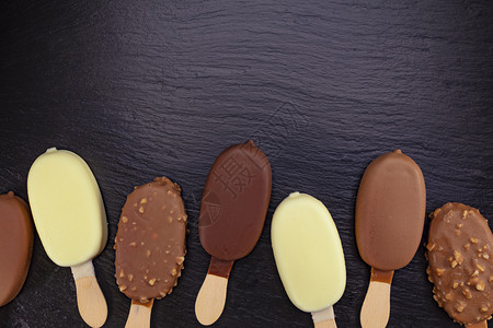 牛奶棍子冰淇淋加粘在木棍上巧克力盖在黑石板上的巧克力乳制品图片