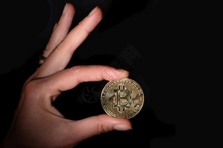 虚拟的金融贸易BitCoin在黑背景的手指之间握有加密货币比特图片