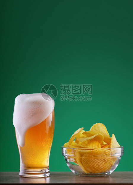 一杯轻啤酒装有滴水泡沫和一块薯片的杯子绿色背景上的一盘芯片杯轻啤酒配有滴水泡沫和碎片板土豆马克杯贮藏啤酒图片