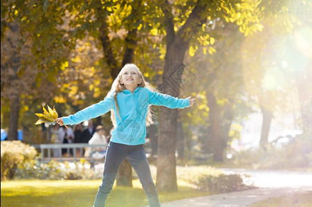 女孩举起她的手臂享受公园的日落秋天树叶女图片