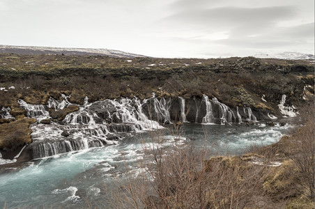 天流动蓝色Hraunfossar瀑布冰地上含蓝水图片