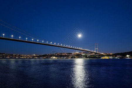 夜晚旅行河博斯普鲁海峡大桥夜间被灯光和月亮照博斯普鲁海峡大桥到岸明亮的月下有灯火通明的房屋土耳其伊斯坦布尔博普鲁海峡大桥夜间被灯图片