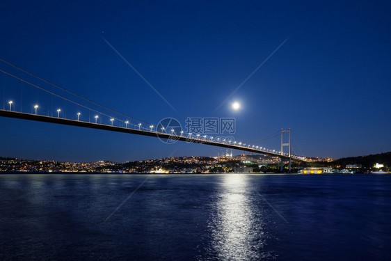 夜晚旅行河博斯普鲁海峡大桥夜间被灯光和月亮照博斯普鲁海峡大桥到岸明亮的月下有灯火通明的房屋土耳其伊斯坦布尔博普鲁海峡大桥夜间被灯图片