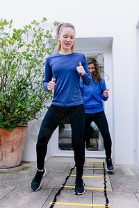 两名年轻妇女在露天台进行快速梯子运动正在做苗条的绑腿图片